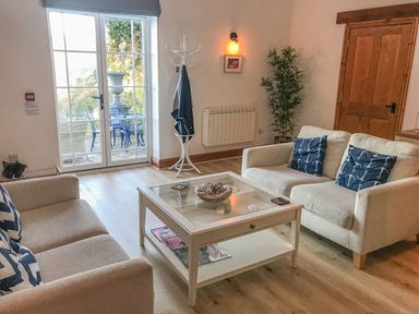 A living room with two beige sofas a glass coffee table and a coat stand near a glass door at Baronet's Quarters in Lynton