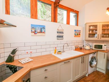 A kitchen with wooden countertop and backsplash tiles a sink microwave and washing machine at Baronet's Quarters in Lynton