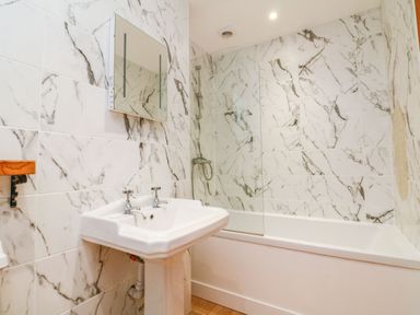 A bathroom with a white sink two taps a mirror bathtub and a shower at Baronet's Quarters in Lynton