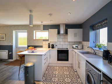 A kitchen with white cabinets a patterned tile floor and a breakfast bar with stools at Eala Bhan Cottage in Clachan near Balivanich