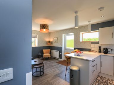 A kitchen and sitting area with chairs tables and a fruit bowl on the counter at Eala Bhan Cottage in Clachan near Balivanich