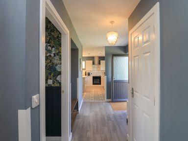 A hallway leading to a kitchen with patterned floor tiles and a blue door at Eala Bhan Cottage in Clachan near Balivanich