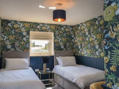 A bedroom with two single beds a window and floral wallpaper at Eala Bhan Cottage in Clachan near Balivanich