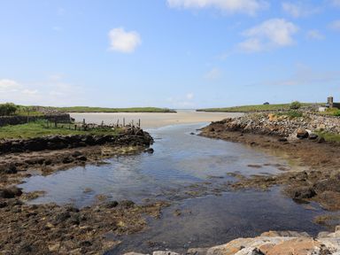 A coastal scene with rocky shoreline and a water channel leading to a sandy beach at Eala Bhan Cottage in Clachan near Balivanich