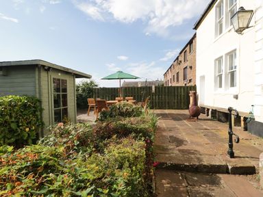 A backyard with a green storage shed wooden patio furniture with an umbrella and a metal chiminea at Abbey Farm House in St Bees