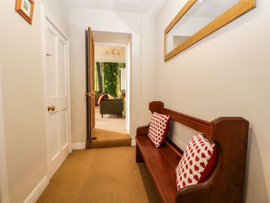 A hallway with a wooden bench and red heart cushions a mirror on the wall and a doorway leading to a room with chairs at Abbey Farm House in St Bees