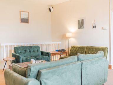 A sitting room with three green sofas a wooden coffee table and side table a floor lamp and framed pictures on the walls at Abbey Farm House in St Bees