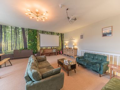 A living room with green sofas a wooden coffee table a projector screen and forest wallpaper at Abbey Farm House St Bees
