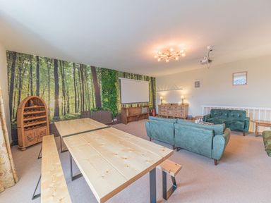 A lounge with wooden tables and benches green couches and a forest mural on the wall at Abbey Farm House in St Bees
