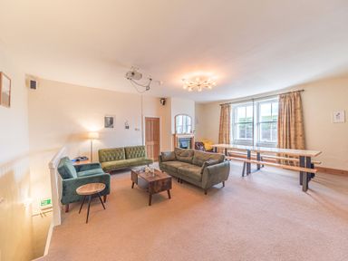 A living room with green sofas a wooden coffee table a dining table with benches and windows with curtains at Abbey Farm House in St Bees