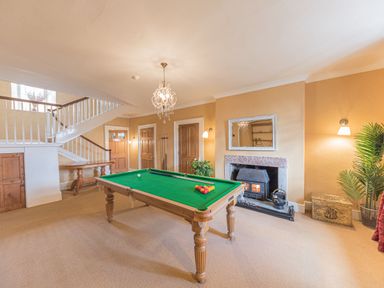 A room with a billiard table, fireplace, chandelier, staircase, wooden doors, and a plant at Abbey Farm House in St Bees