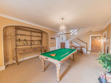 A game room with a pool table, wooden shelves, coat rack, staircase, and a wooden door at Abbey Farm House in St Bees