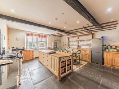 A kitchen with a large island table chairs wooden cabinets and two refrigerators at Abbey Farm House in St Bees