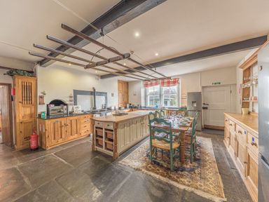 A kitchen with wooden cabinets a central island and a dining table with green chairs at Abbey Farm House in St Bees