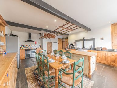 A kitchen with a wooden dining table set with dishes and green chairs at Abbey Farm House in St Bees