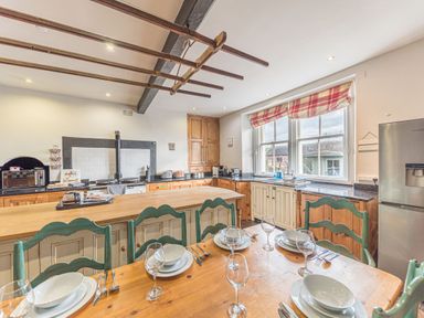 A kitchen with a wooden dining table set with plates and glasses a countertop with appliances and cabinets by a window at Abbey Farm House in St Bees