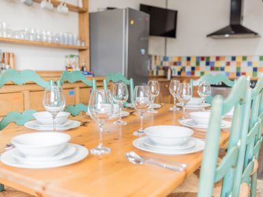 A dining table set with white plates bowls and wine glasses in a kitchen with green chairs and colorful tiled backsplash at Abbey Farm House in St Bees