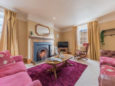 A living room with sofas, a wooden coffee table, a fireplace, rocking chair, television, and curtains at Abbey Farm House in St Bees