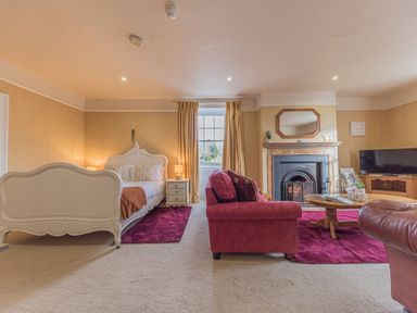 A bedroom and sitting area with a white bed red sofa fireplace and television at Abbey Farm House in St Bees