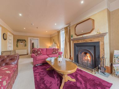 A living room with a lit fireplace red sofas a wooden coffee table and a purple rug at Abbey Farm House in St Bees
