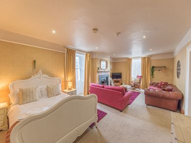 A bedroom with a white bed and sofa seating area with red and brown sofas by windows and fireplace at Abbey Farm House in St Bees
