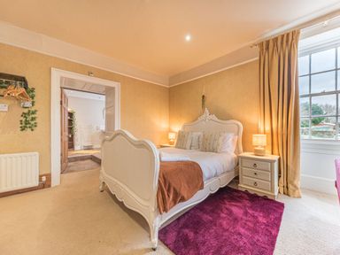 A bedroom with a white bed and bedside tables with lamps a purple rug and a large window at Abbey Farm House in St Bees