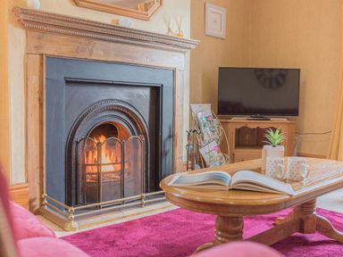 A living room with a fireplace a coffee table with an open book two mugs and a plant a television and a magazine rack at Abbey Farm House in St Bees