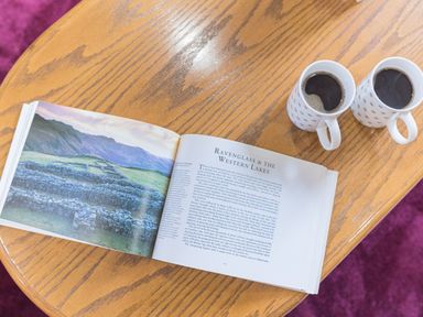 A wooden table with an open book showing ruins and text and two mugs of black coffee at Abbey Farm House in St Bees