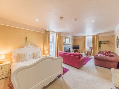 A bedroom and living area with a white bed a red sofa a checker chair TV and fireplace at Abbey Farm House in St Bees