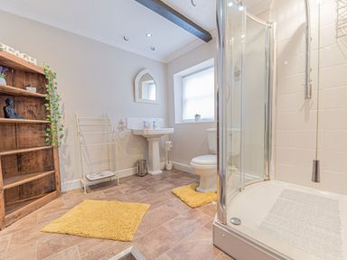 A bathroom with a shower enclosure toilet pedestal sink wooden shelf and two yellow rugs at Abbey Farm House in St Bees