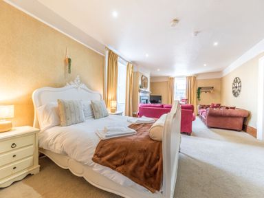 A bedroom with a white bed, bedside tables with lamps, red sofas, a television, and windows with curtains at Abbey Farm House in St Bees