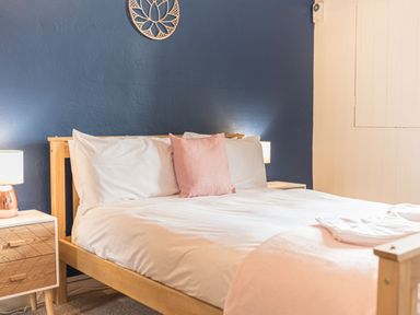 A bedroom with a wooden bed frame white bedding a pink pillow two bedside tables with lamps and a blue wall at Abbey Farm House in St Bees