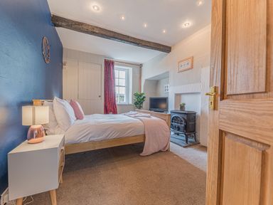 A bedroom with a bed side table and lamp a wood stove and television at Abbey Farm House in St Bees