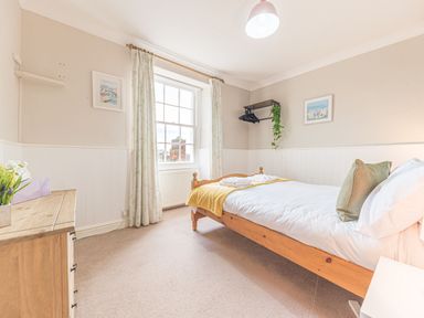 A bedroom with a wooden bed and white bedding next to a window with curtains and a wooden chest of drawers at Abbey Farm House in St Bees