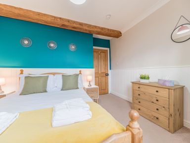 A bedroom with a wooden bed and green pillows a wooden dresser with a plant and tissue box and a blue accent wall at Abbey Farm House in St Bees