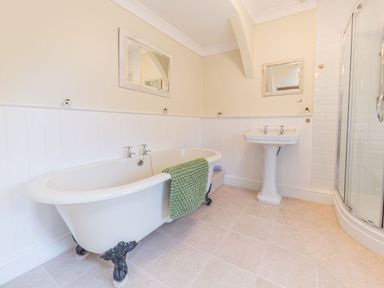 A bathroom with a clawfoot bathtub a green towel a pedestal sink two mirrors and a glass shower at Abbey Farm House in St Bees