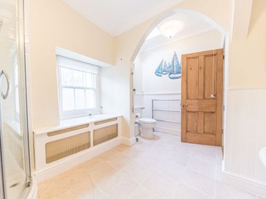 A bathroom with a corner shower cubicle a wooden door a toilet under an archway and a window with a radiator cover at Abbey Farm House in St Bees