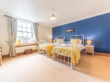 A bedroom with two single beds yellow blankets and pillows a blue accent wall and a window with curtains at Abbey Farm House in St Bees