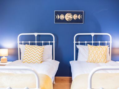 A bedroom with two white metal beds with yellow patterned cushions and a lamp on each side at Abbey Farm House in St Bees