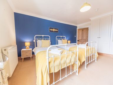 A bedroom with two single beds with yellow blankets and pillows a blue accent wall with a moon phase artwork a wooden door white wardrobes and bedside tables with lamps at Abbey Farm House in St Bees