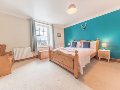 A bedroom with a wooden bed with white bedding and blue pillows a wooden chest and a side table with lamps at Abbey Farm House in St Bees
