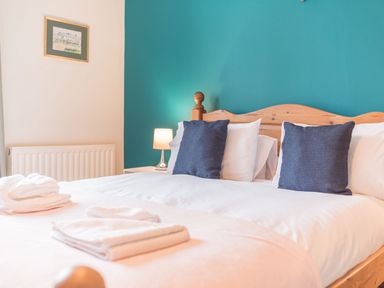 A bedroom with a wooden bed with white bedding and dark cushions a bedside lamp and picture on the wall at Abbey Farm House in St Bees
