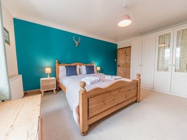 A bedroom with a wooden bed, bedside tables with lamps, blue accent wall, and white wardrobes at Abbey Farm House in St Bees