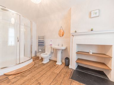 A bathroom with a curved glass shower, a toilet, a sink, a towel rack, and open shelving at Abbey Farm House in St Bees