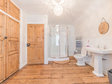 A bathroom with wooden floors wooden doors a shower toilet sink and a round mirror at Abbey Farm House in St Bees