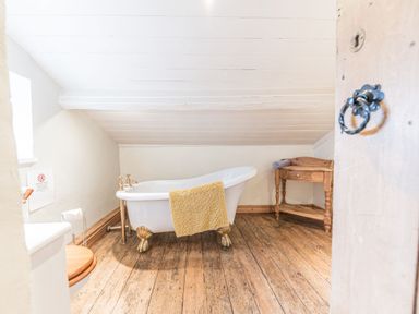 A bathroom with a clawfoot bathtub wooden floor and a wooden side table at Abbey Farm House in St Bees