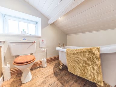 A bathroom with a toilet that has a wooden seat and a clawfoot bathtub with a yellow bath mat at Abbey Farm House in St Bees