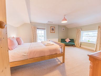 A bedroom with a wooden bed with pink pillows and blanket a green sofa with a pink cushion and two windows with curtains at Abbey Farm House in St Bees
