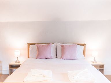 A double bed with pink cushions white bedding and bedside tables with lamps at Abbey Farm House in St Bees
