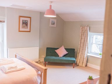 A bedroom with a wooden bed, green sofa with pink cushion, framed pictures on walls and a window with curtains at Abbey Farm House in St Bees